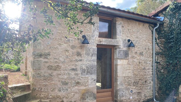 Un bâtiment en pierre avec une porte en bois, deux lampes fixées au mur et une petite fenêtre.