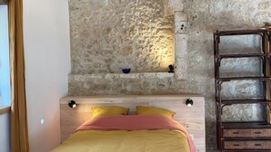 Une chambre avec un lit, un plancher en bois, un mur en pierre et une étagère.