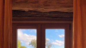 Une pièce avec un plafond en bois, une fenêtre donnant sur un champ verdoyant et un mur en pierre.