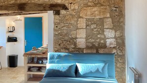 Une pièce avec un mur en pierre, un canapé bleu, une table en bois et une porte bleue.