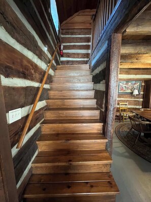 A wooden staircase with a handrail, wooden walls, and a dining area with chairs and a table.