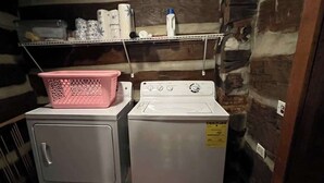 A laundry area with a washing machine and dryer, a pink laundry basket, and shelves with various items. - Blackberry Inn at Heritage Farm (Huntington)