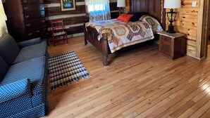 A log cabin bedroom with a bed, dresser, and a blue patterned sofa. - Blackberry Inn at Heritage Farm (Huntington)