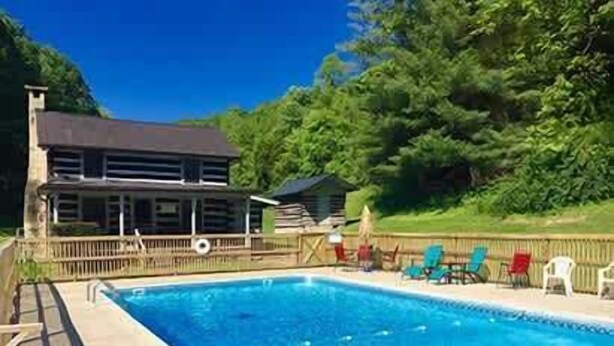 A swimming pool with lounge chairs, a wooden deck, and a building with a dark roof. - Blackberry Inn at Heritage Farm (Huntington)