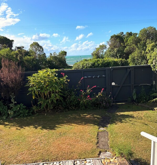 A garden with a pathway leading to a gate, surrounded by lush greenery and a view of the sea.