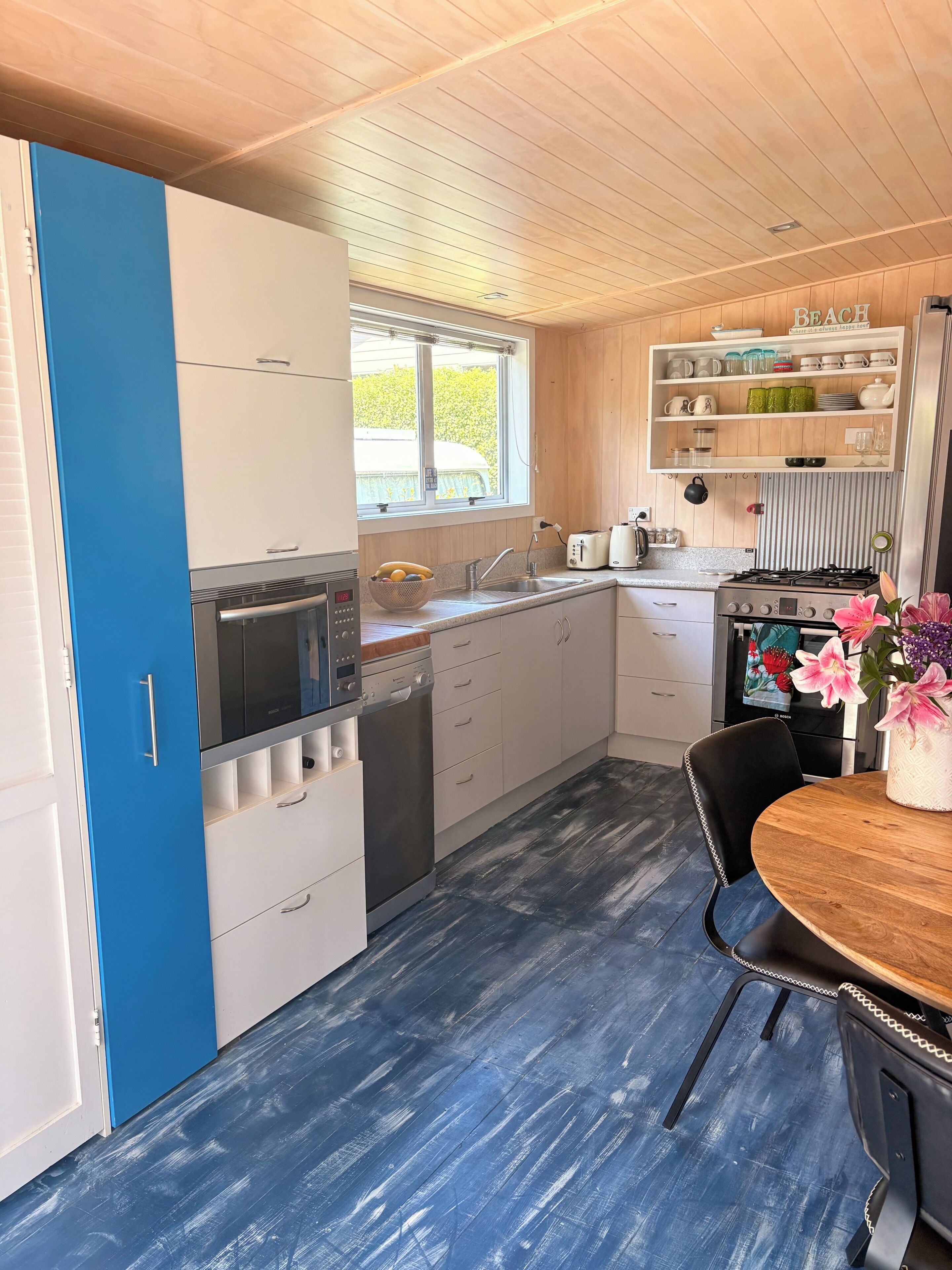 A kitchen with a blue door, white cabinets, a window, and a dining area with a table and chairs.