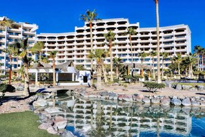 Ein großes Hotel mit zahlreichen Balkonen, einem Poolbereich mit Felsen und Palmen.