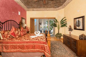 Ein Schlafzimmer mit einem großen Bett, einem Holzkopfteil, einer roten Wand, einer großen Pflanze und Blick durch eine Glastür.