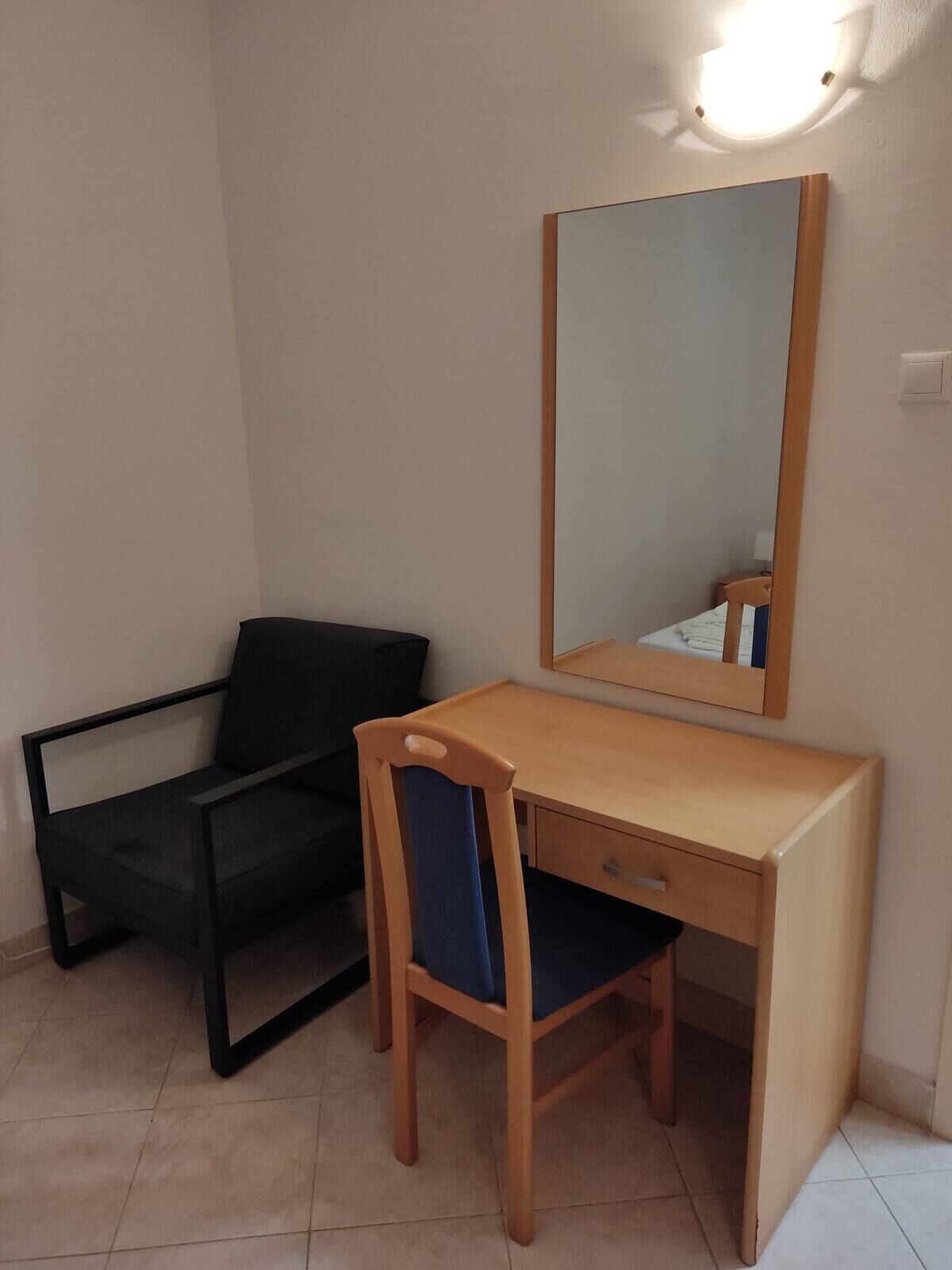 Une pièce comprenant un bureau en bois, une chaise, un canapé noir et un miroir fixé au mur.