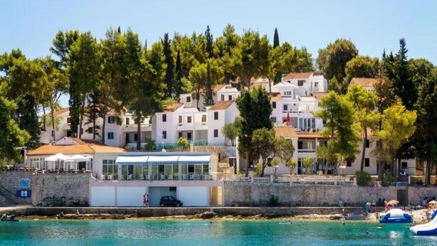 A coastal hotel with multiple white buildings, a stone wall, and a clear view of the sea. - Apartment F1 in Lumbarda with pool near beach (Lumbarda)