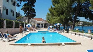 A swimming pool with lounge chairs and umbrellas, surrounded by trees and buildings. - Apartment F1 in Lumbarda with pool near beach (Lumbarda)