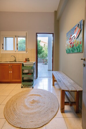 A kitchen with cabinets, a sink, a window, a green cart, a wooden bench, and a painting on the wall. - Armonia-Art House (Kos)