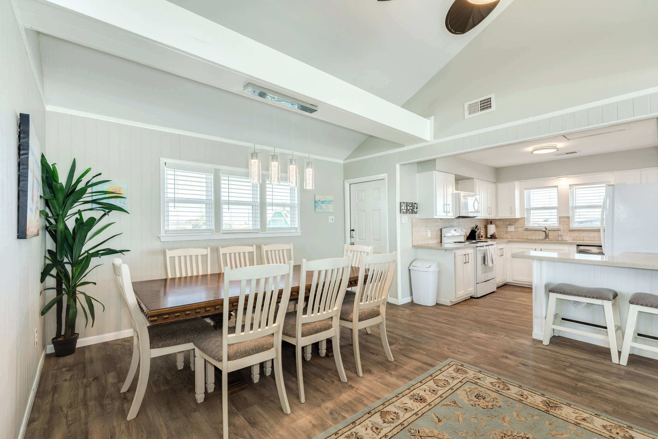 A spacious kitchen with white cabinets, a dining area with a wooden table and chairs, and a large potted plant.