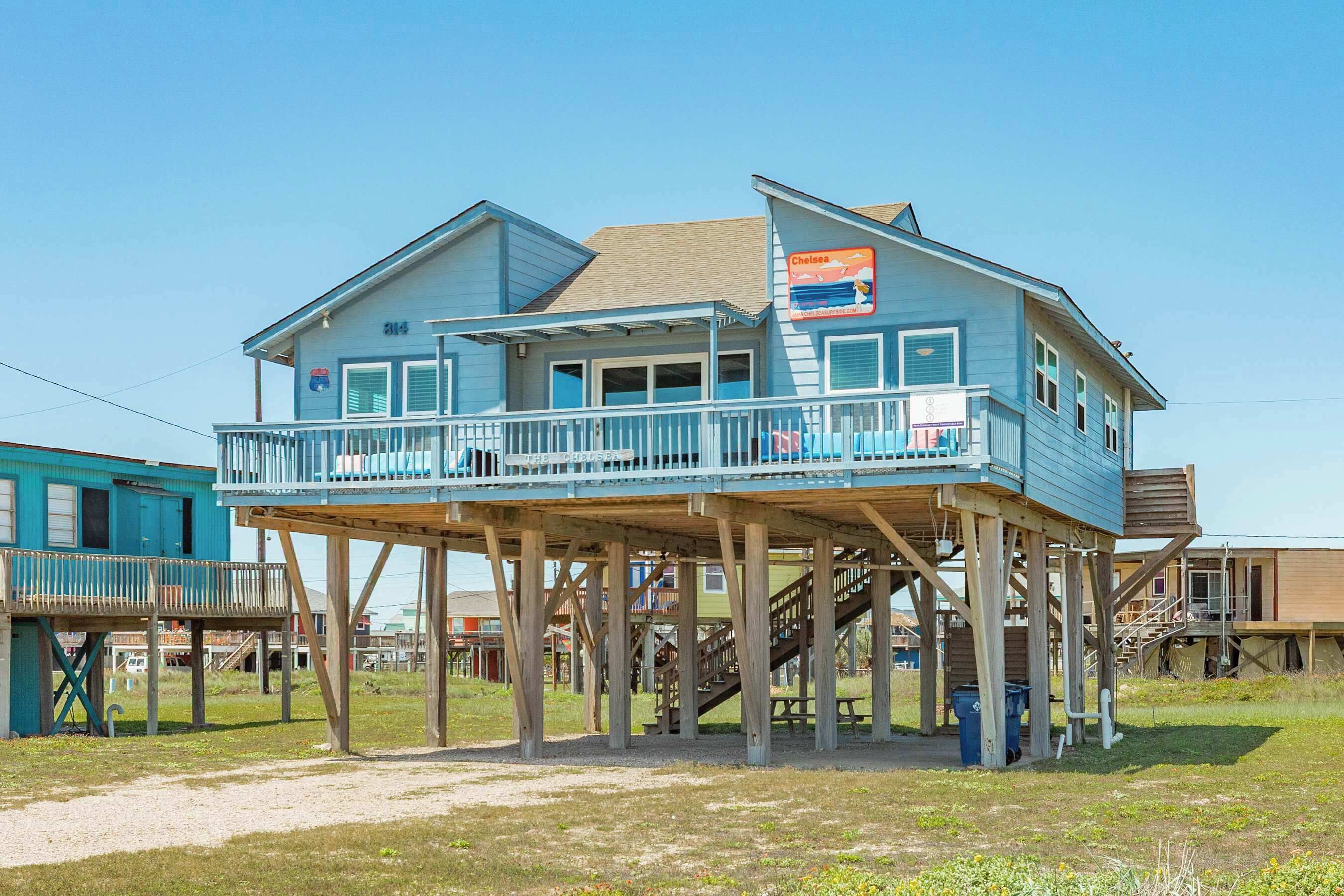 A two-story house with a balcony on the upper floor, wooden stilts supporting the structure, and a sign advertising a seafood restaurant.