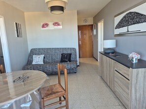 Ein Wohnzimmer mit einer Couch, einem Esstisch mit Stühlen, einer Küchenzeile mit Arbeitsplatte und Schränken sowie einem Flur, der zu einer Tür führt.