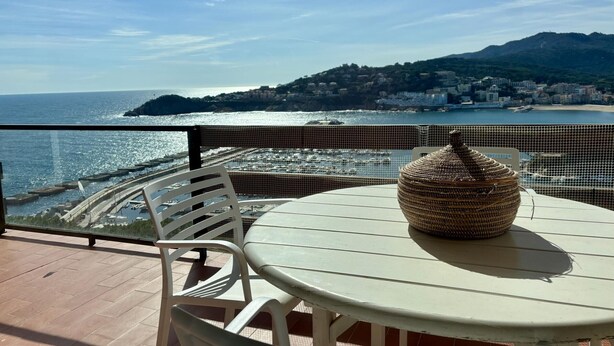 Un balcone con vista sul mare, un vaso di vimini e sedie bianche.