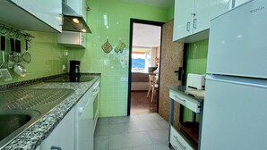 Una cucina compatta con un piano di lavoro in granito, mobili bianchi e vista su una sala da pranzo attraverso un'apertura.