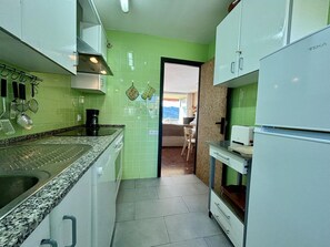 Cuina compacta amb taulell de granat, armaris blancs i vista cap a una zona de menjador a través d'una porta oberta.