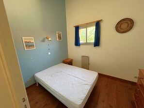 A bedroom with a single bed, a small wooden table, a radiator, a window with curtains, and wall-mounted pictures. - Duplex apartment, sea view, parking - 4 guests (Argelès-sur-Mer)