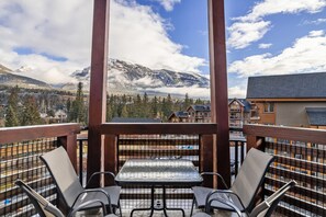 A balcony with a view of snow-capped mountains, a table, and chairs. - Luxury Penthouse Unparalleled Views & Comfort (Canmore)