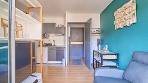 A compact living space with a kitchenette, a grey sofa, a TV, and a teal accent wall. - Studio in Barbotan-les-Thermes, Wi-Fi, Pets Allowed (Barbotan-les-Thermes)