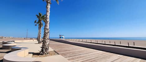 A coastal promenade with palm trees, a wooden boardwalk, and a clear view of the beach.