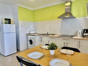 A compact kitchen with a washing machine, a microwave, and a toaster. There is a dining table set with plates, wine glasses, and cutlery. - Comfortable apartment in Canyelles with terrace and parking, near the beach (Roses)