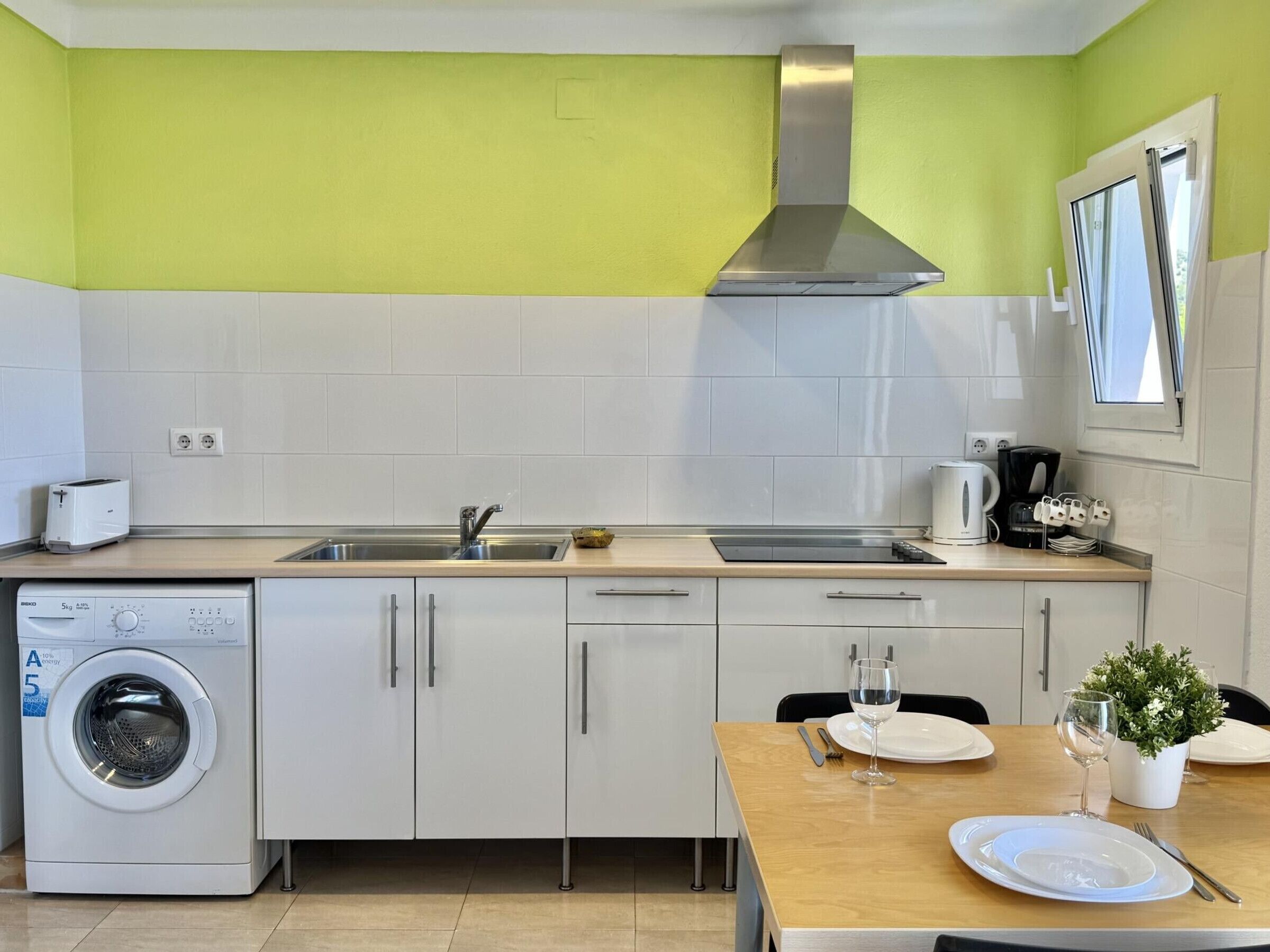 A compact kitchen with a washing machine, a sink, a stove, and a dining area with a table set for two.