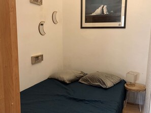Ein Schlafzimmer mit einem Bett, Kissen, einem gerahmten Bild, einem Nachttisch und einem kleinen Holzschemel.