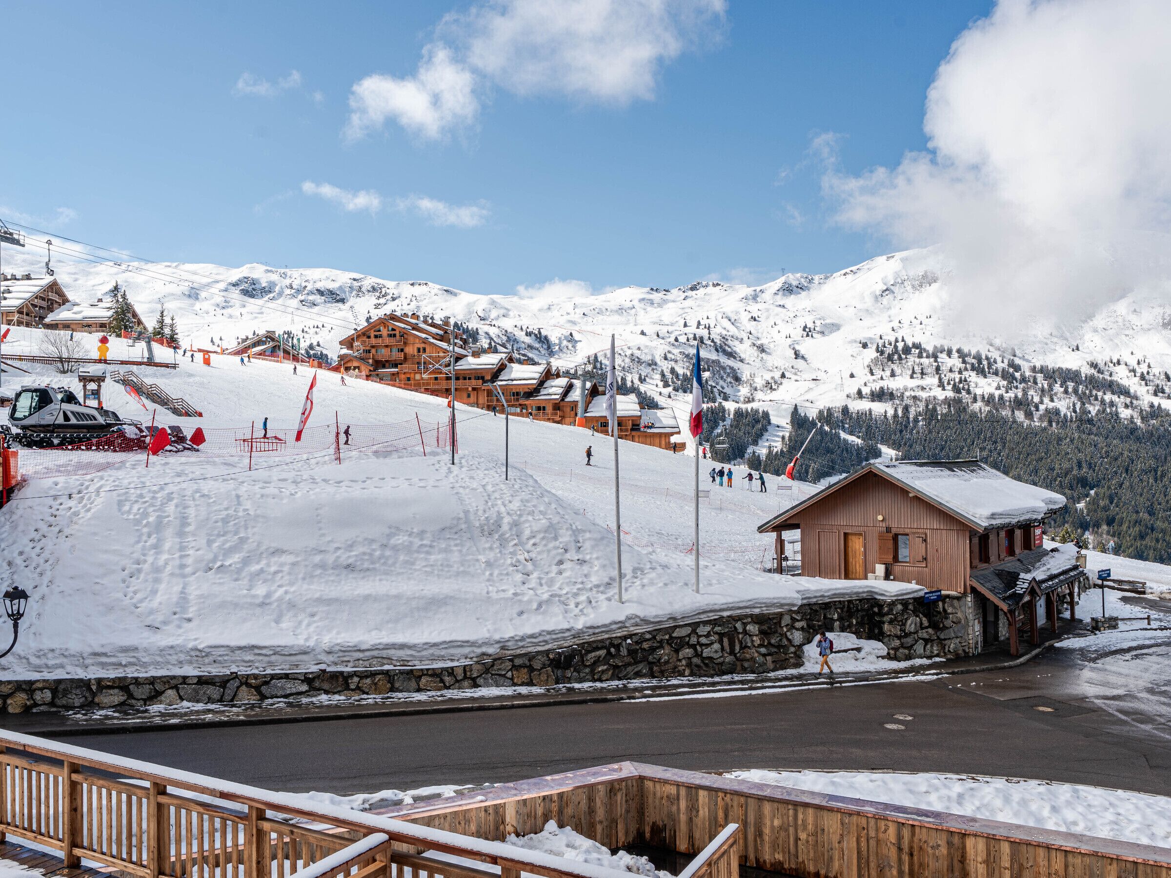 A snow-covered mountain resort with wooden buildings, ski slopes, and a clear sky.