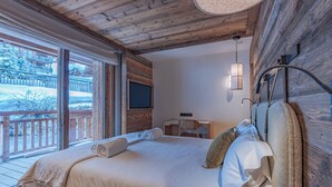 Ein Schlafzimmer mit Holzboden, einem Bett mit Kissen, einem Schreibtisch, einem Stuhl und einem an der Wand befestigten Fernseher.
