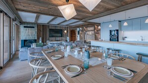 Ein geräumiger Essbereich mit einem langen Holztisch, gedeckt für eine Mahlzeit, eine Küche mit modernen Geräten und ein großer Fernseher an der Wand.