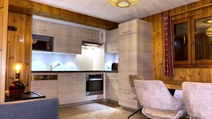 A modern kitchen with wooden cabinets, a built-in oven, and a dining area with two chairs. - Charming apartment in village center - 4 guests (La Clusaz)