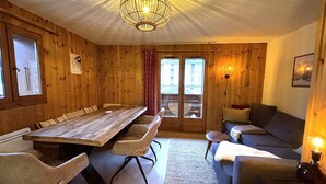 A wooden interior with a long dining table, chairs, a sofa, and a chandelier. - Charming apartment in village center - 4 guests (La Clusaz)