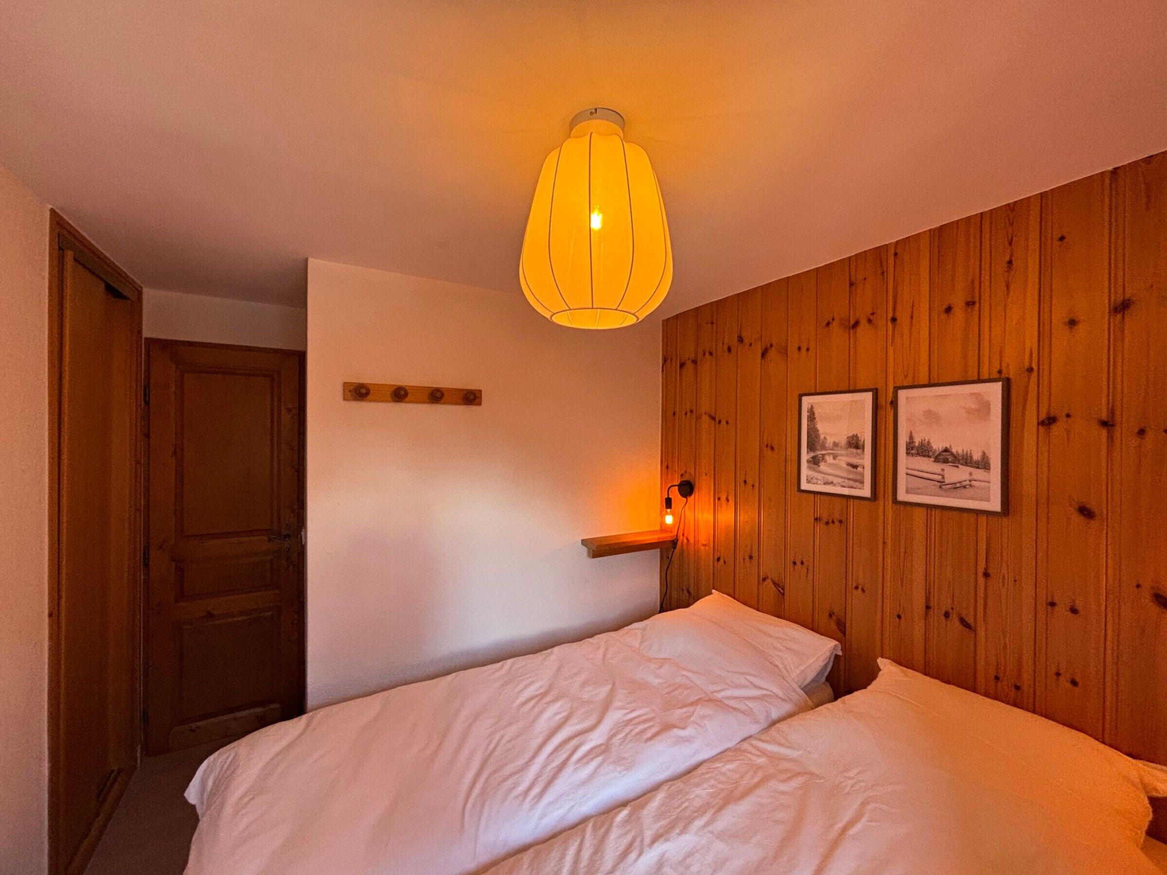 A bedroom with a wooden wall, a bed, a bedside table, and a hanging light fixture.