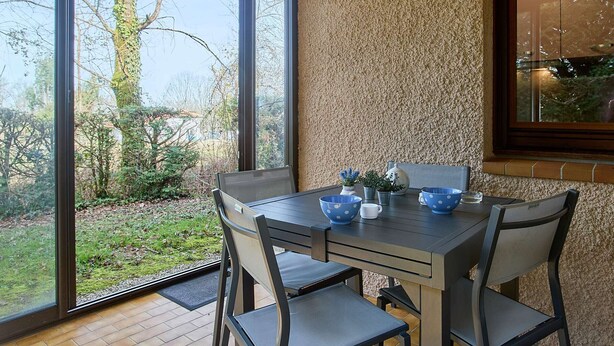 Ein Essbereich mit Tisch und Stühlen, Blick ins Freie und einer strukturierten Wand.