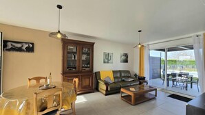 Una sala de estar con una mesa de comedor, un sofá, un armario y un ventanal corredero que da a un espacio al aire libre.