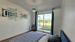 Un dormitorio con cama, una silla, un ventanal con cortinas y decoración en la pared.