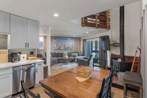 Eine moderne Küche mit Edelstahlgeräten, ein Essbereich mit einem Holztisch und ein Wohnzimmer mit einer Couch und einem großen Gemälde.