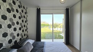 Une chambre avec un mur orné d’un motif géométrique, un lit avec une literie à rayures et une vue sur un espace extérieur accessible par une porte-fenêtre coulissante.