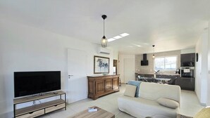 Un salon moderne doté d’un téléviseur à écran plat, d’un meuble en bois, d’un canapé et d’un coin repas avec une table en verre.
