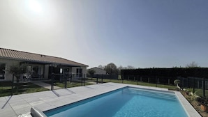 Une piscine avec une terrasse carrelée, un patio couvert et une cour clôturée.