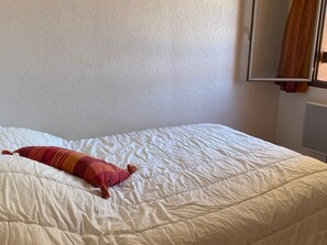 Un lit avec une couette blanche et un oreiller rayé de rouge et d’orange.