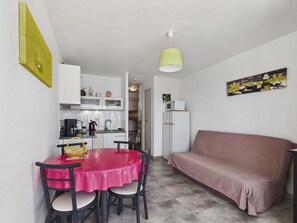 A compact living space with a kitchenette, a dining area with a red table and chairs, and a pink sofa. - Renovated studio cabin, sea view - 4 guests (Le Grau d'Agde)