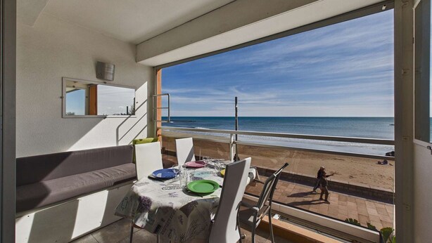 En balkon med et spisebord, der giver udsigt over en strand.