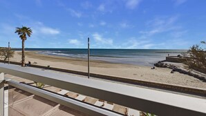 Strandudsigt fra en balkon med en palme, klar himmel og en sandstrand.