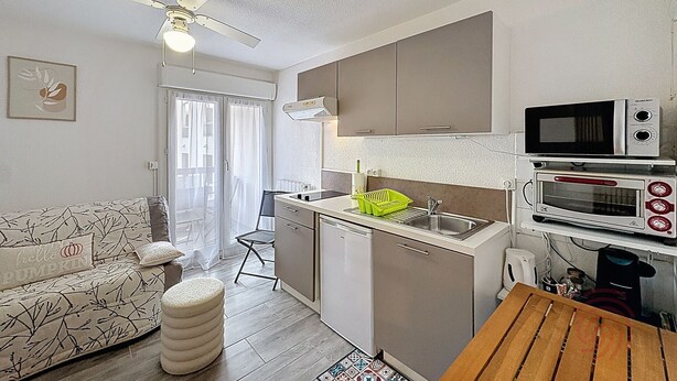 A compact kitchen with a microwave, oven, and sink. There's a small dining area with a table and a sofa. A ceiling fan is visible. - Studio, pets welcome, near city center (Lamalou-les-Bains)
