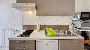 A compact kitchen with a built-in microwave, a stove, a sink, and a dishwasher. - Studio, pets welcome, near city center (Lamalou-les-Bains)