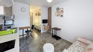 A compact room with a ceiling fan, a bed, a desk with a chair, a television, and a small shelf with decorative items. - Studio, pets welcome, near city center (Lamalou-les-Bains)