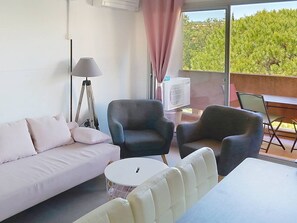 A modern room with a sofa, two armchairs, a small round table, a lamp, and a large window with a view of greenery. - Air-conditioned studio cabin - Bormes-les-Mimosas (Bormes-les-Mimosas)
